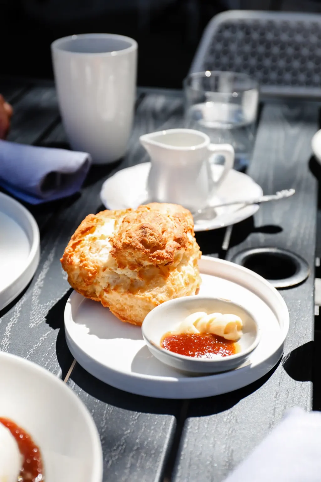 A golden buttermilk biscuit with butter and jam on a sunny patio table
