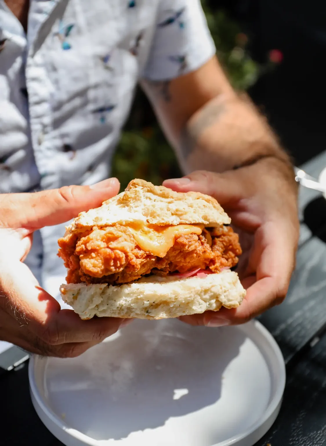 Hands holding a fried chicken sandwich on a biscuit